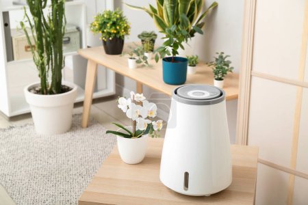 Photo for Modern humidifier and flowers in pot on table in interior of living room - Royalty Free Image