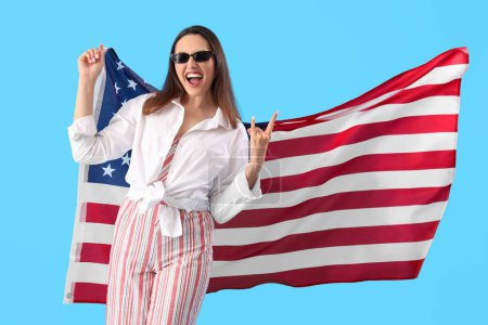 Téléchargez les photos : Jeune femme avec le drapeau des États-Unis montrant "cornes du diable" sur fond bleu - en image libre de droit