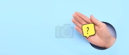 Téléchargez les photos : Main féminine et papier collant avec point d'interrogation sur fond bleu clair avec espace pour le texte - en image libre de droit