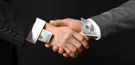 Foto de Empresarios con soborno estrechando las manos sobre fondo oscuro - Imagen libre de derechos