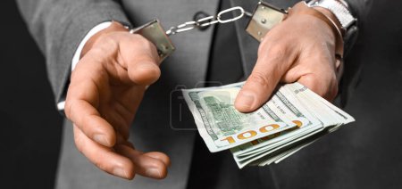 Handcuffed businessman with bribe on dark background, closeup