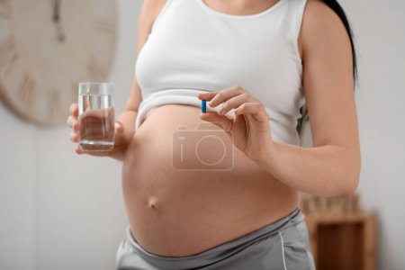 Photo for Pregnant woman with Folic Acid pill and glass of water at home, closeup - Royalty Free Image