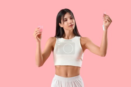 Young woman with menstrual cup and tampon on pink background