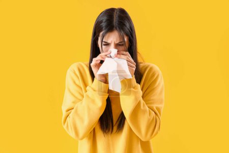 Téléchargez les photos : Jeune femme allergique avec éternuement tissulaire sur fond jaune - en image libre de droit