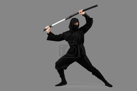 Männlicher Ninja mit Schwert auf grauem Hintergrund