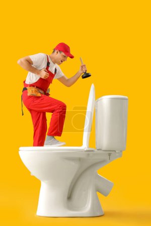 Photo for Young plumber with plunger and toilet bowl on yellow background - Royalty Free Image