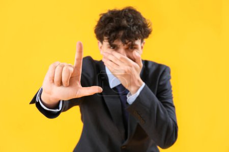 Photo for Laughing businessman showing loser gesture on yellow background - Royalty Free Image