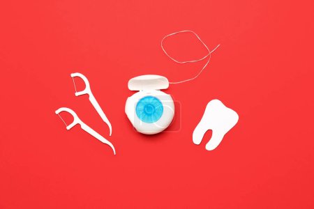 Hilo dental, palillos y modelo de dientes sobre fondo rojo