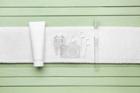 Foto de Toalla con palillos de dientes de hilo dental, cepillo, pasta de dientes y modelo de dientes de plástico sobre fondo de madera verde - Imagen libre de derechos