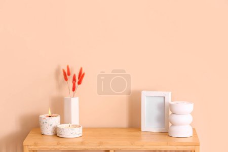 Photo for Holders with burning candles and blank frame on table near beige wall in room - Royalty Free Image
