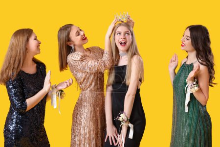 Young women crowning prom queen on yellow background