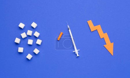 Téléchargez les photos : Cubes de sucre avec seringue pour injection d'insuline et flèche dirigée vers le bas sur fond bleu - en image libre de droit
