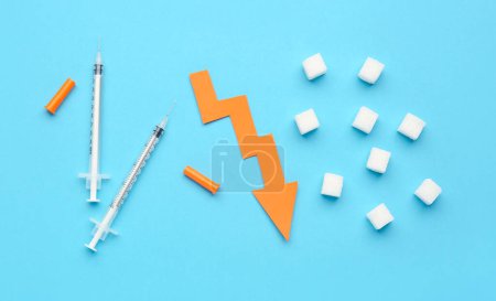 Téléchargez les photos : Sucre avec seringues pour injection d'insuline et flèche dirigée vers le bas sur fond bleu - en image libre de droit