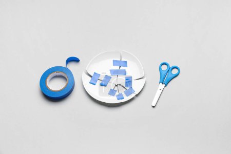 Photo for Broken plate with adhesive tape and scissors on light background - Royalty Free Image