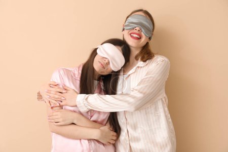 Téléchargez les photos : Amis féminines dans les masques de sommeil étreignant sur fond beige - en image libre de droit