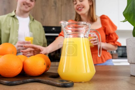 Jug of juice with oranges on table in kitchen, closeup