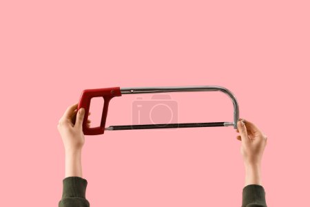 Téléchargez les photos : Mains féminines tenant une scie à métaux sur fond rose - en image libre de droit