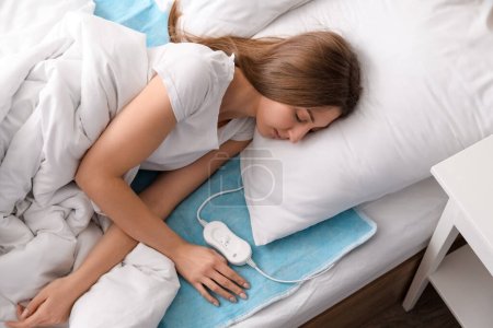 Photo for Young woman sleeping on electric heating pad in bedroom - Royalty Free Image
