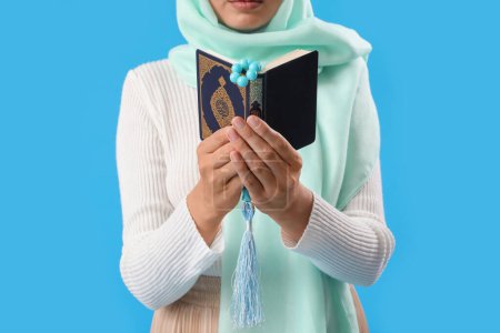 Téléchargez les photos : Jeune femme musulmane avec coran et perles de prière sur fond bleu, gros plan. Fête du Nouvel An islamique - en image libre de droit