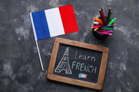 Chalkboard with text LEARN FRENCH, flag and pen cup on dark background-stock-photo