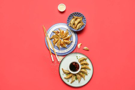 Photo for Plates with tasty Chinese jiaozi and sauce on red background - Royalty Free Image