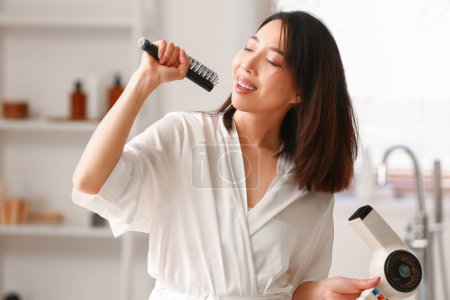 Photo for Pretty young Asian woman drying hair and singing in bathroom - Royalty Free Image