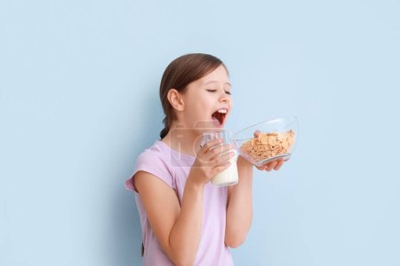 Photo for Little girl with milk and cornflakes on light blue background - Royalty Free Image
