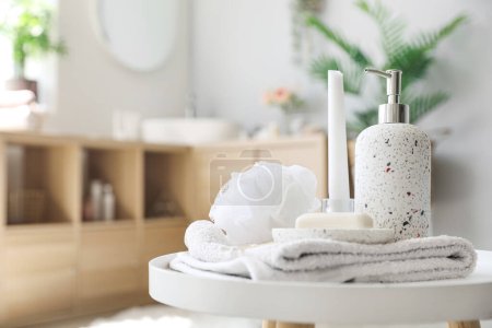 Soap bar, dispenser, shower sponge, towel and candle on table in bathroom, closeup