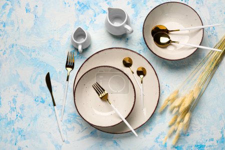 Photo for Clean plates with golden cutlery and dried lagurus on blue grunge table - Royalty Free Image