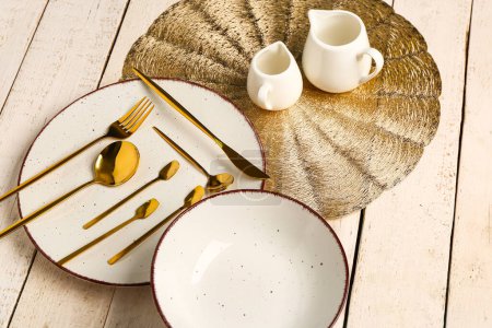 Photo for Clean plate, set of golden cutlery, bowl and pitchers on white wooden table - Royalty Free Image