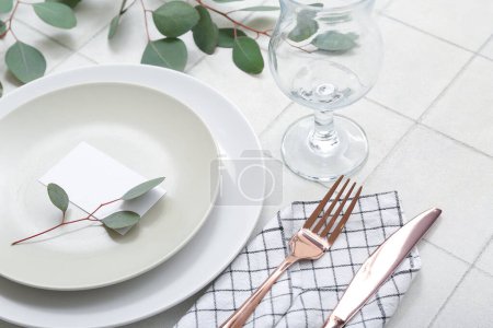 Foto de Hermosa mesa con tarjeta de invitación en blanco y ramas de eucalipto en mesa de azulejos blancos - Imagen libre de derechos
