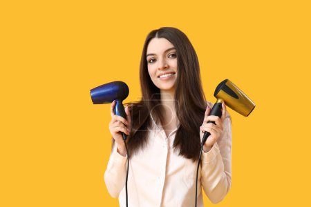 Photo for Beautiful young woman with hair dryers on yellow background - Royalty Free Image