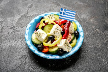 Foto de Cuenco de ensalada con queso feta, aceitunas y bandera griega sobre mesa grunge negra - Imagen libre de derechos