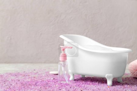 Photo for Small bathtub with foam, bottle of cosmetic product and sea salt on grunge background - Royalty Free Image