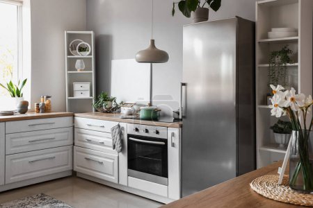 Téléchargez les photos : Intérieur de la cuisine légère avec réfrigérateur élégant, comptoirs et étagères - en image libre de droit