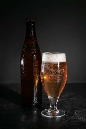 Flasche und Glas kaltes Bier auf dunklem Hintergrund