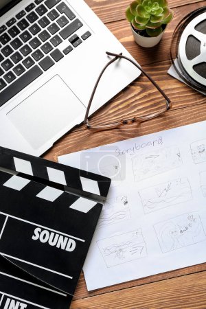 Photo for Storyboard with movie clapper, laptop and eyeglasses on wooden background - Royalty Free Image