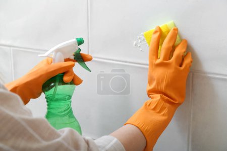 Foto de Mujer con guantes de goma limpiando baldosas ligeras con esponja, bicarbonato de sodio y pulverizador, primer plano - Imagen libre de derechos