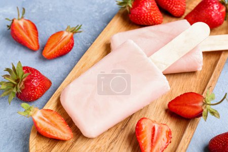Photo for Wooden board with sweet strawberry ice-cream popsicles on blue background - Royalty Free Image