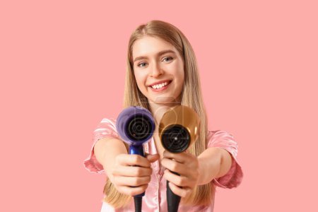 Photo for Young blonde woman in pajamas with hair dryers on pink background - Royalty Free Image