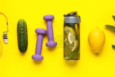 Téléchargez les photos : Bouteille de limonade sportive avec concombre et haltères sur fond jaune - en image libre de droit