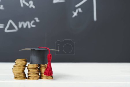 Foto de Tapa de graduación y pilas de monedas en la mesa blanca contra pizarra. Concepto de préstamo estudiantil - Imagen libre de derechos