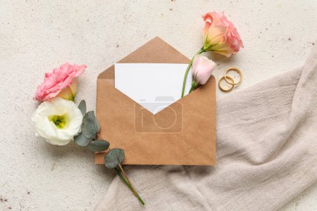 Foto de Composición con sobre, tarjeta en blanco, anillos de boda y flores de eustoma sobre fondo claro - Imagen libre de derechos