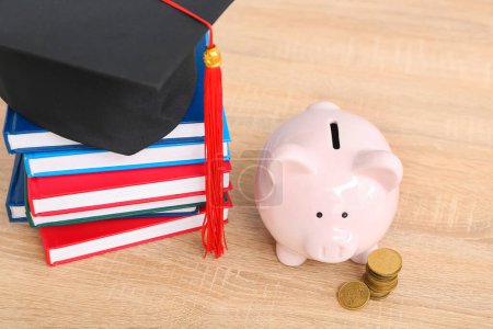 Piggy bank, stack of coins, books and graduation hat on wooden background. Student loan concept