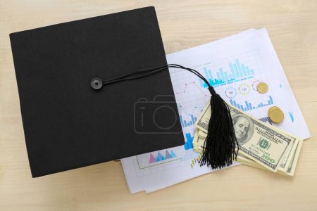 Foto de Tapa de graduación, billetes de dólar, monedas y hoja de papel con gráficos sobre fondo de madera. Concepto de préstamo estudiantil - Imagen libre de derechos