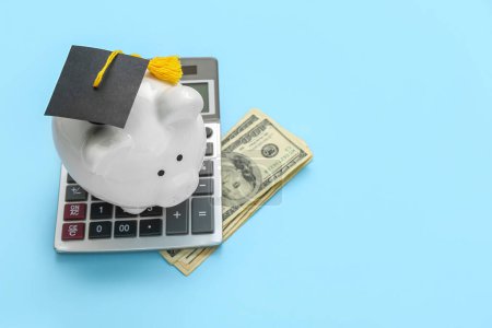 Foto de Hucha en gorra de graduación, calculadora y billetes de dólar sobre fondo azul. Concepto de préstamo estudiantil - Imagen libre de derechos