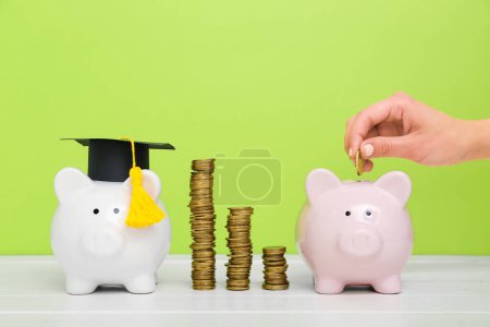 Woman putting coin into piggy bank on white table against green background. Student loan concept