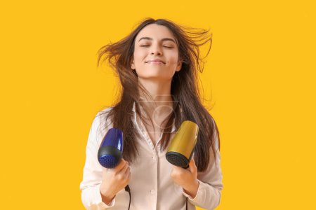 Photo for Beautiful young woman with hair dryers on yellow background - Royalty Free Image