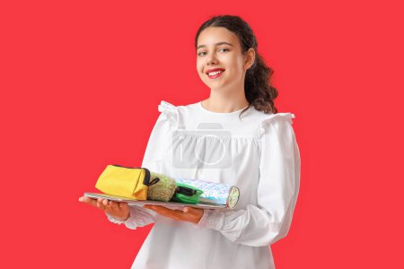 Photo for Female student with pencil cases and laptop on red background - Royalty Free Image