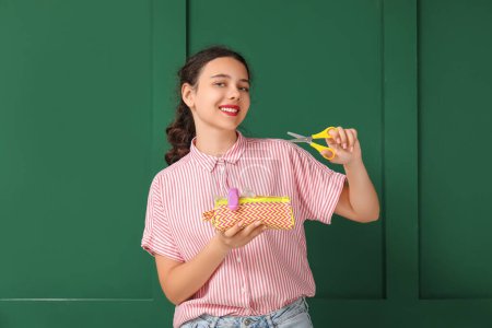 Photo for Female student with scissors and pencil case on green background - Royalty Free Image